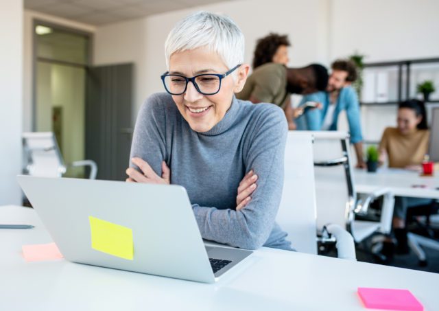 3 façons de surmonter les préjugés générationnels au travail, femme âgées regardant son ordinateur dans un open space, souriante et attentive, L'effet A